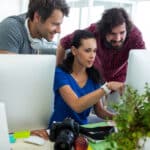 Drei Personen arbeiten gemeinsam als Mediengestalter am Computer.