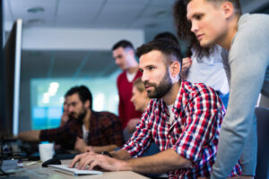 IT Umschüler schauen als Gruppe auf einen Computer.