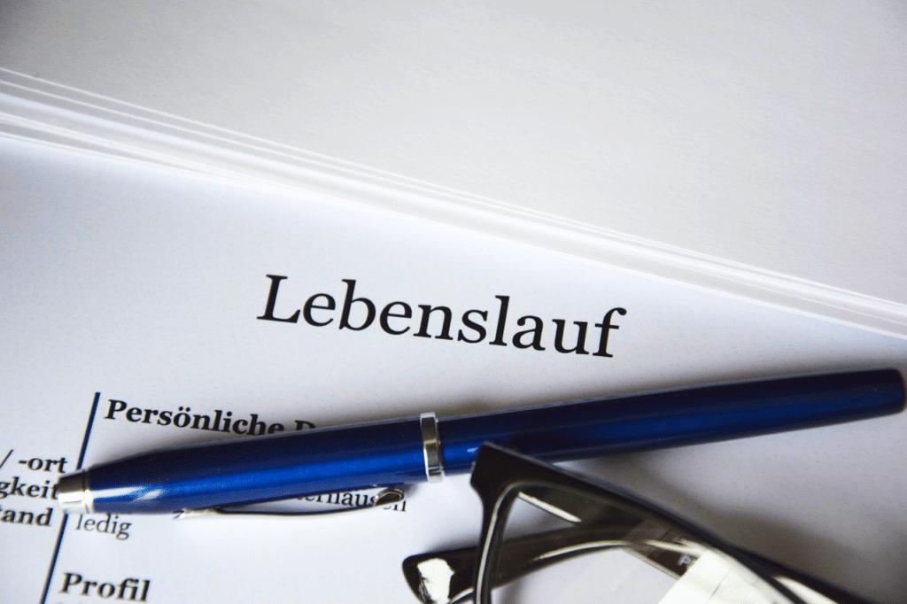 Ein Lebenslauf ist zu sehen, darauf ein Kugelschreiber und eine Lesebrille.
