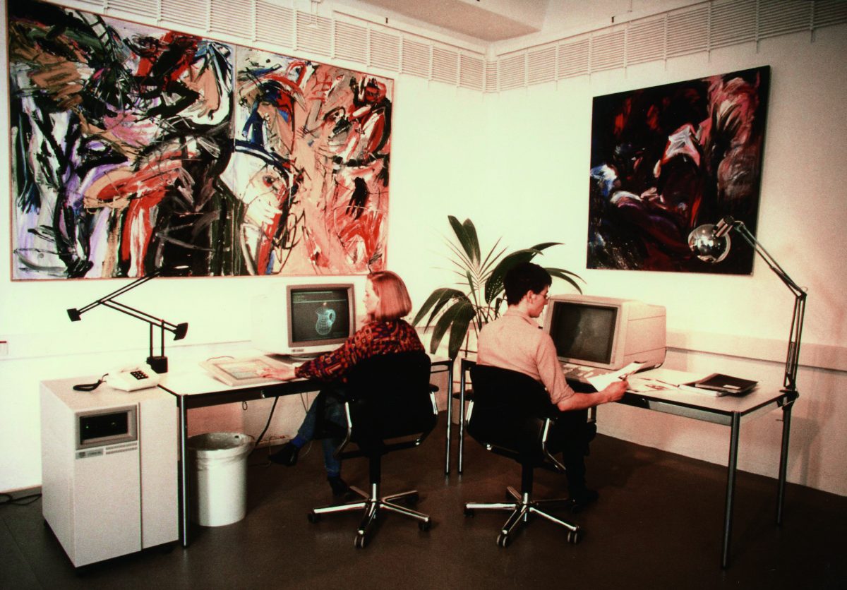Zwei Personen sitzen an Schreibtischen und sind am PC, während ihrer Grafik Designer Ausbildung.