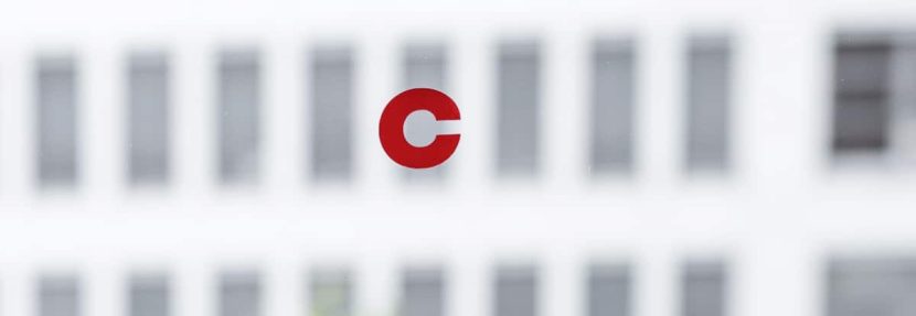 Rotes cimdata-Logo auf Glas mit einem Gebäude im Hintergrund.