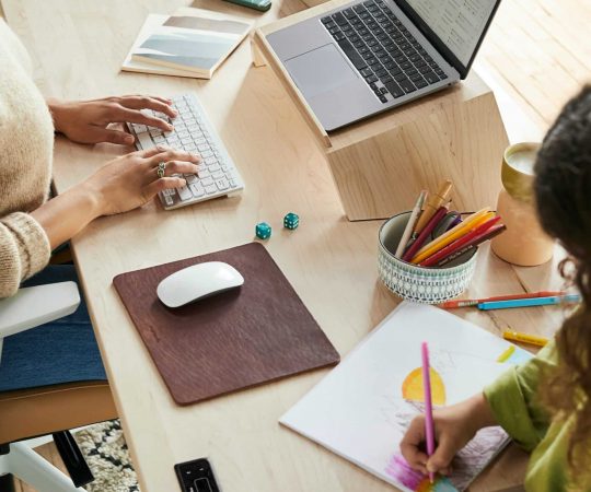 Frau arbeitet an Schreibtisch während Kind malt
