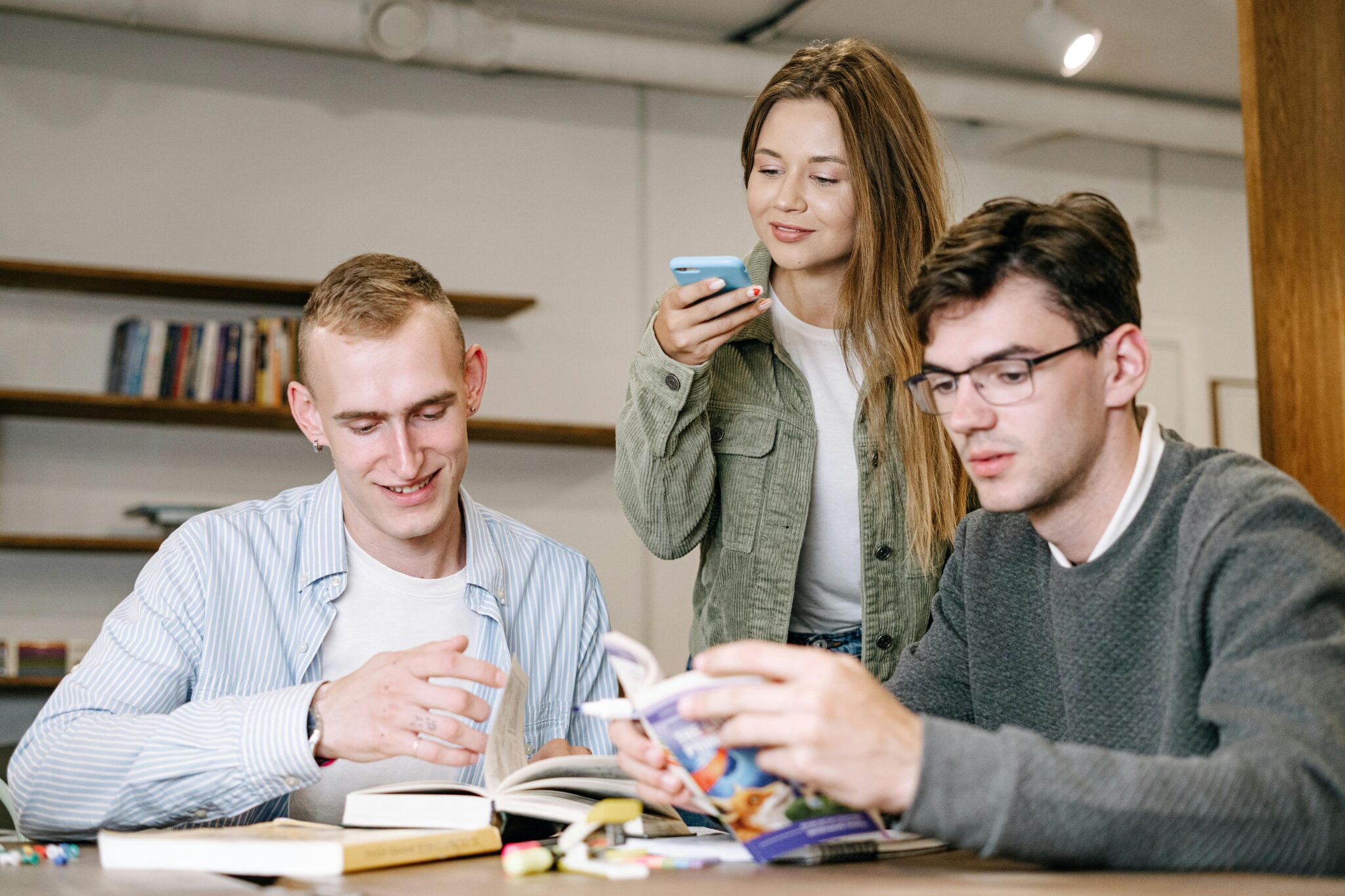 Eine Frau macht mit Handy ein Bild während zwei Männer mit Büchern arbeiten