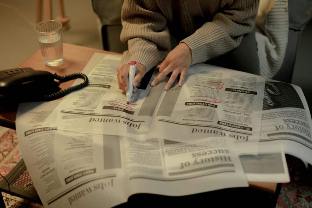 Eine Person markiert Stellenanzeigen in einer Zeitung mit einem roten Stift.